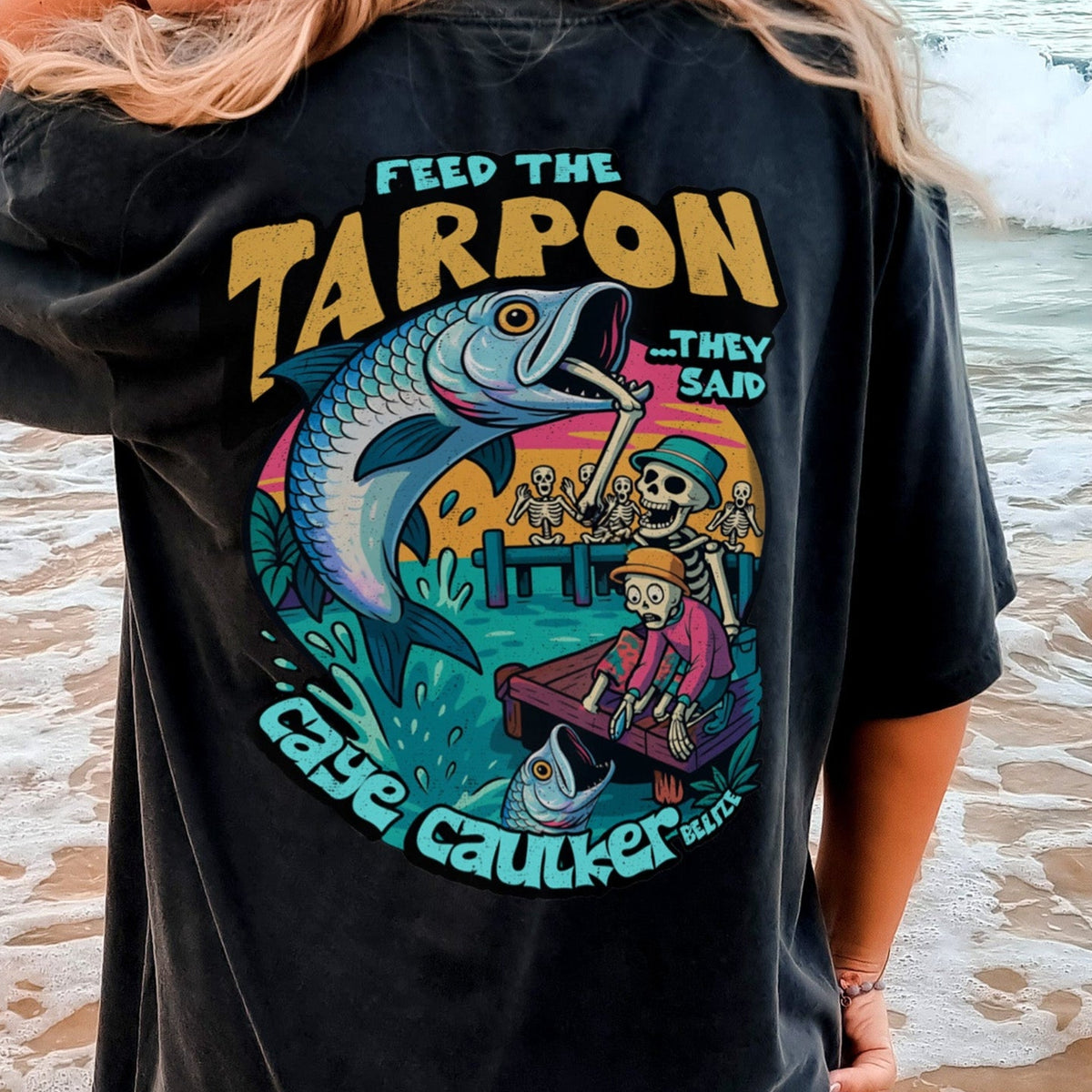 Person wearing a black t-shirt with a colorful graphic of skeletons and tarpon on the beach in Caye Caulker, Belize